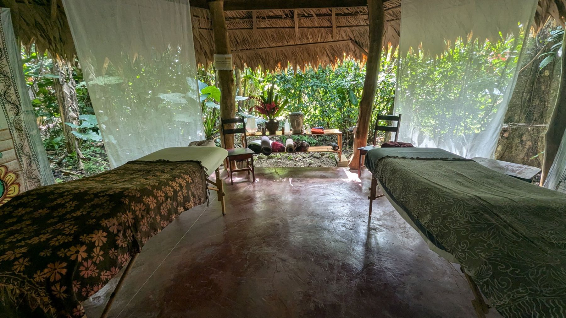Two massage tables in a thatched open-air hut surrounded by jungle